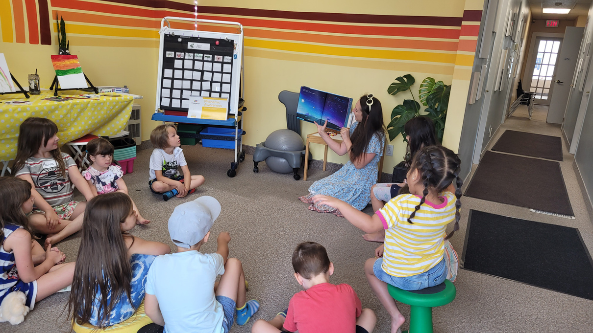 a group of children sitting on the floor in for a story for the literacy day camp